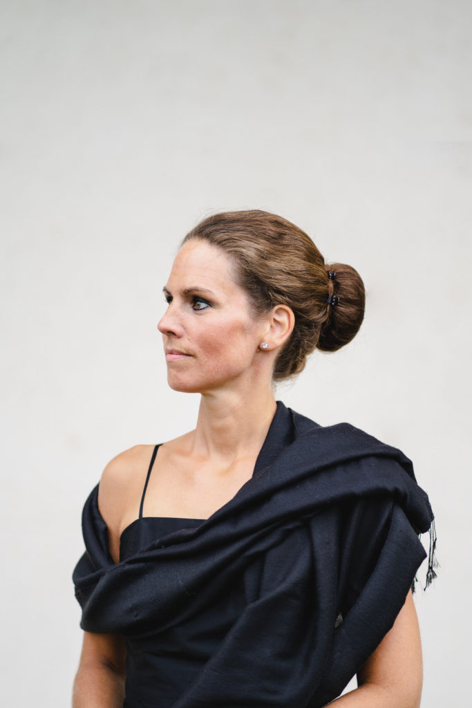Charlotte Schmidt-Berger mit schwarzem Kleid und eleganter Frisur vor grauem Hintergrund